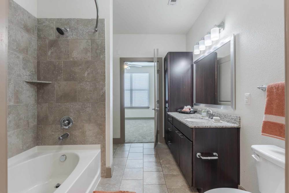 Interior view of a bathroom with a bath tub, sink, toilet, and cabinets located at Henley at The Rim in San Antonio, Texas.