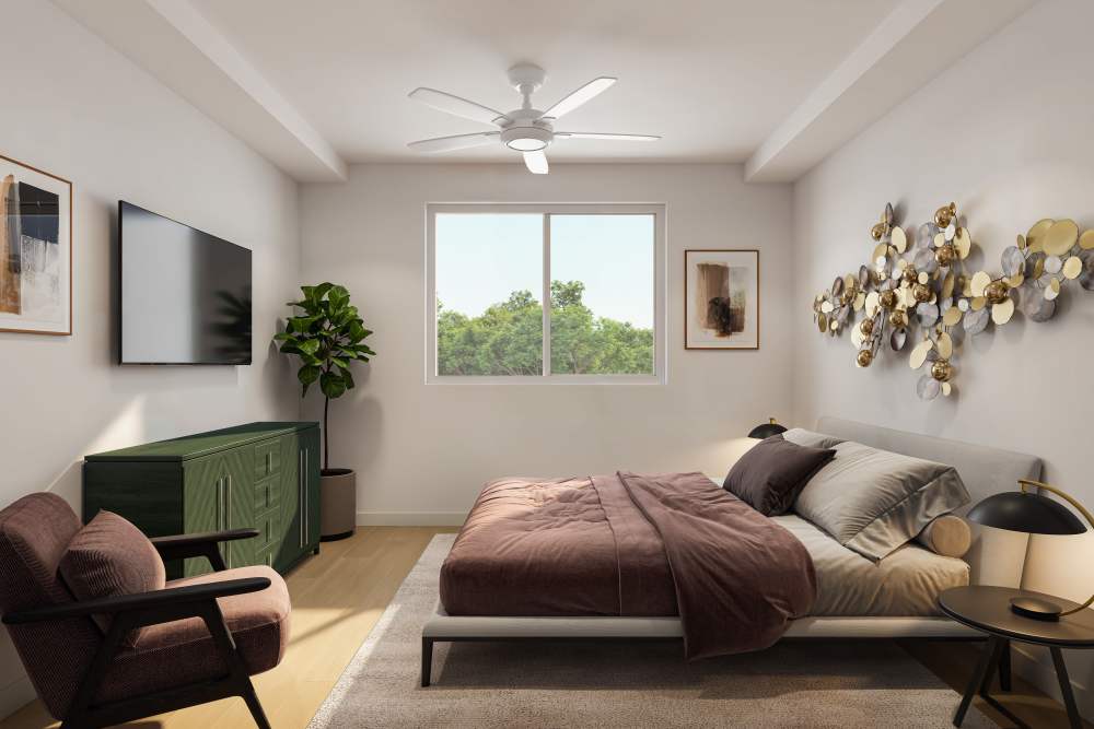 Cozy bedroom featuring a queen-sized bed with soft linens, a ceiling fan, a green dresser, and a large window providing natural light and a view of greenery outside at The Renaissance in Naples, Florida
