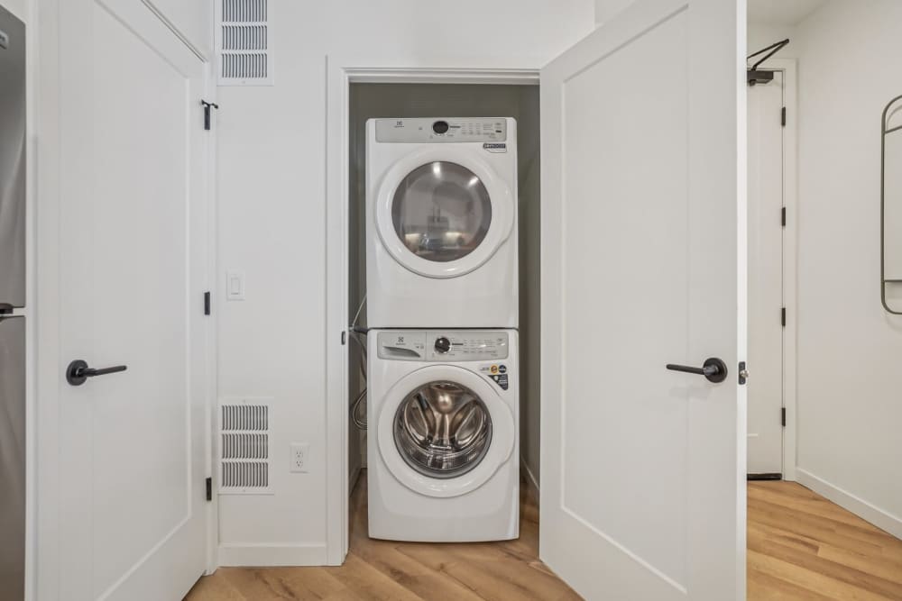 Stacked washer and dryer units in a clean laundry area, featuring white walls and wooden flooring at Tempo at Nine Mile Station in Aurora, Colorado