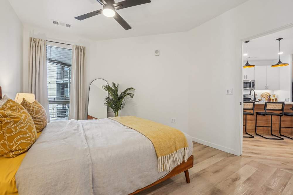 Bedroom with a large bed adorned with yellow accents, a window with curtains, and a decorative plant at Tempo at Nine Mile Station in Aurora, Colorado.