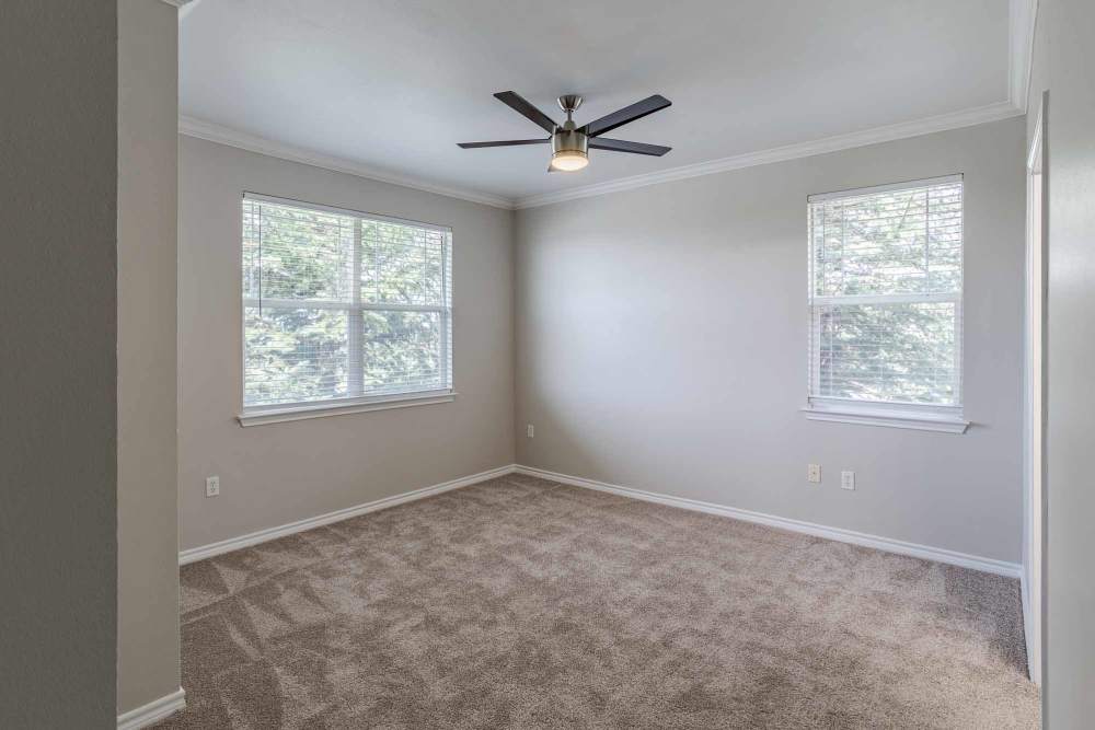 Cozy living space with soft carpeting, large windows for natural light, a ceiling fan, and a private balcony door, at Bella Springs Apartments in Colorado Springs, Colorado.D