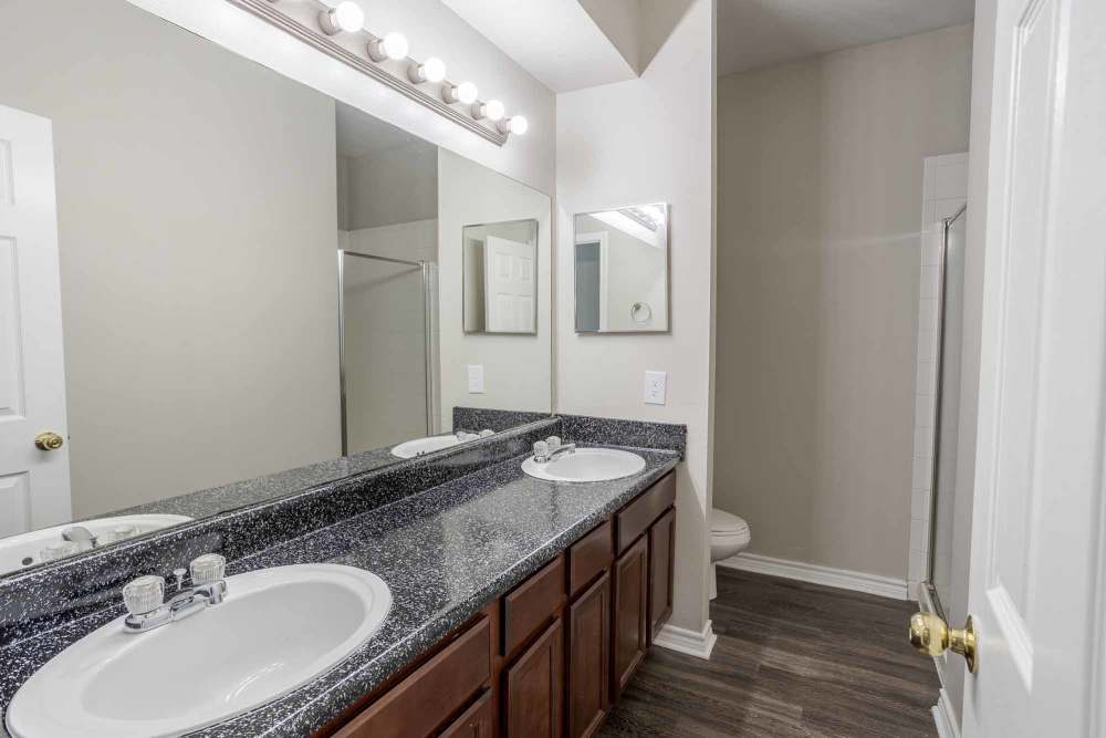 Modern bathroom featuring a dual sink vanity with granite countertops, bright lighting, and mirrors, at Bella Springs Apartments in Colorado Springs, Colorado.