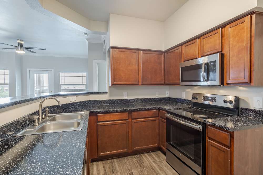 Stylish kitchen with dark wood cabinetry, granite countertops, and modern appliances, featuring a view into the living area, at Bella Springs Apartments in Colorado Springs, Colorado