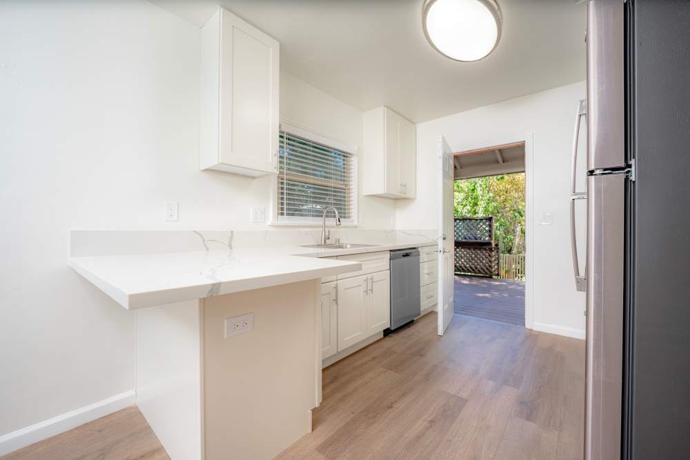 Bright and airy kitchen with white cabinetry and countertops, featuring an open layout that leads to an outdoor area, at Copa Cabanas in Santa Cruz, California.