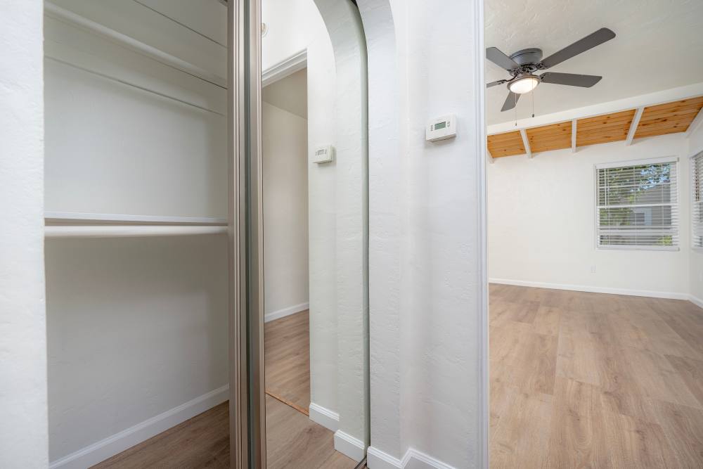 Interior view of a closet with mirrored doors and shelves, leading to a spacious room with a ceiling fan, at Copa Cabanas in Santa Cruz, California.