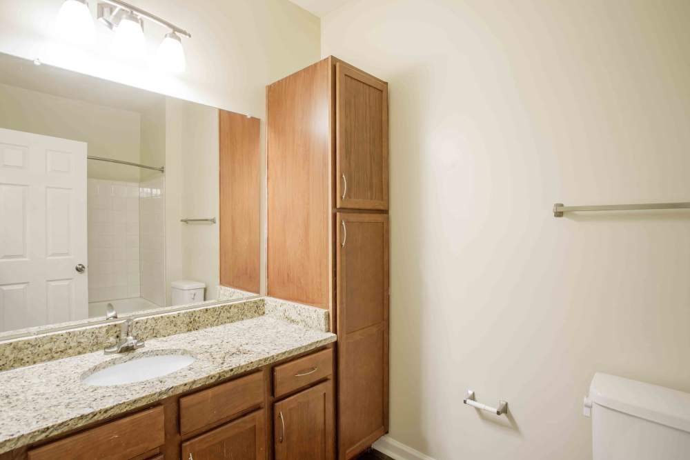Bathroom with granite countertop, wooden cabinets, mirror, and shower area at Commonwealth at 31 in Spring Hill, Tennessee.