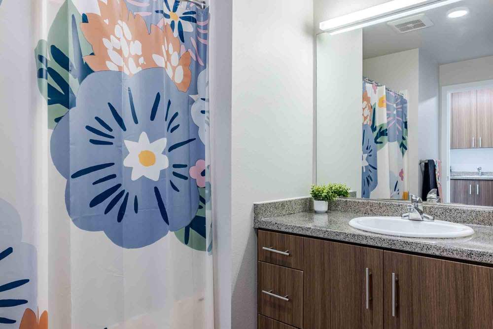 Bathroom with floral curtain separating the shower and sink with mirror at Willow Creek Crossing in Hillsboro, Oregon