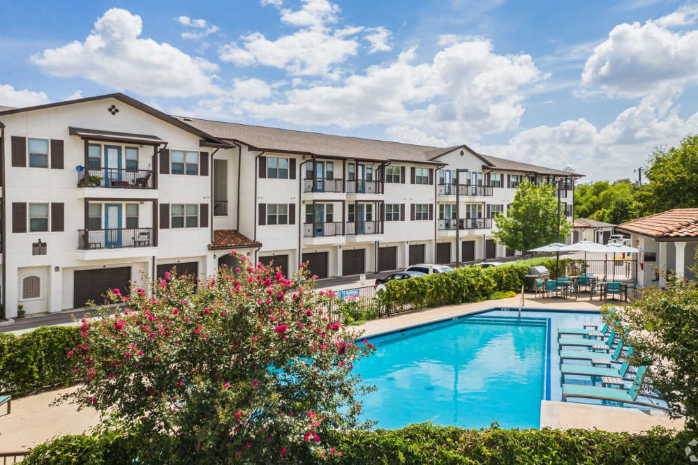 Modern apartments overlooking a sparkling pool and lush landscaping at Alcove at Alamo Heights in San Antonio, Texas
