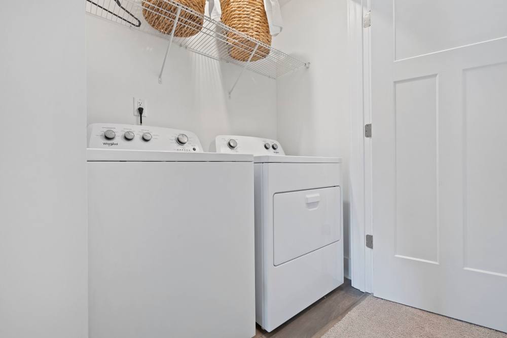 Laundry room with white washer and dryer and storage shelf at Artisan Living Mills River in Mills River, North Carolina