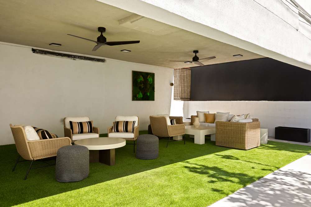 Outdoor lounge area with chairs, tables under a covered patio with grass carpet at The Indie Glendale Collection in Glendale, California