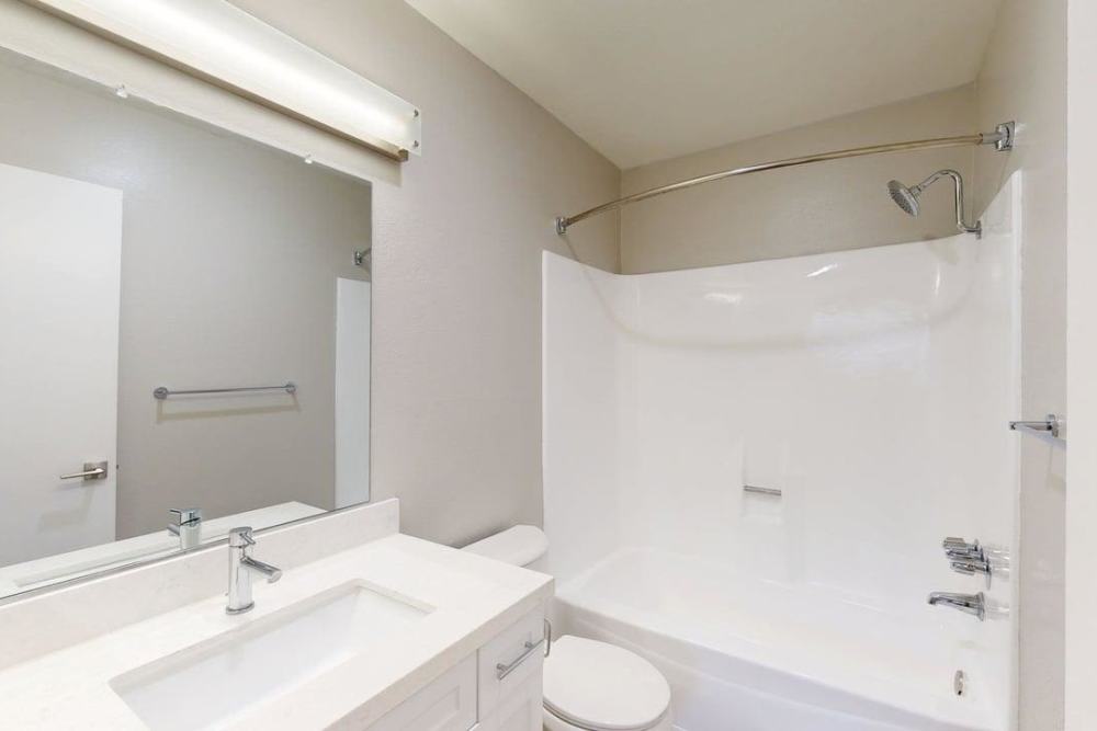 Bright bathroom with vanity lights, white cabinetry, shower and tub , large mirror and a commode at The Indie Glendale Collection in Glendale,California