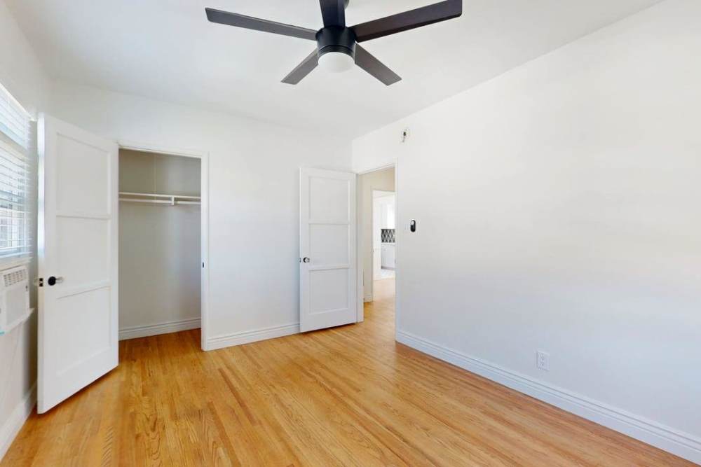 Empty bedroom showing a walkin closet with wood flooring and a black ceiling fan at The Indie Glendale Collection in Glendale, California