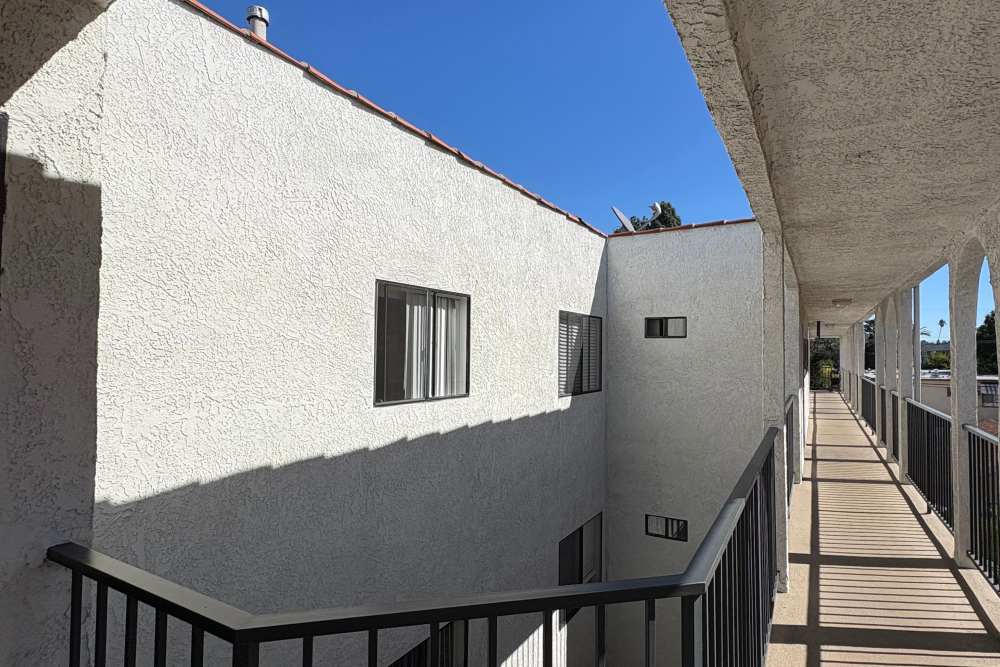 Exterior corridor of a white stucco apartment building with black railings, bright sunlight, and clear blue sky at The Indie Glendale Collection in Glendale, California