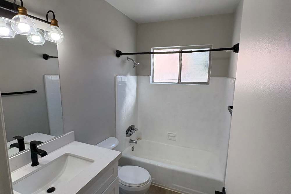 Bright bathroom with White flush sink, black faucet, vanity lights, commode and soaking tub at The Indie Glendale Collection in Glendale, California