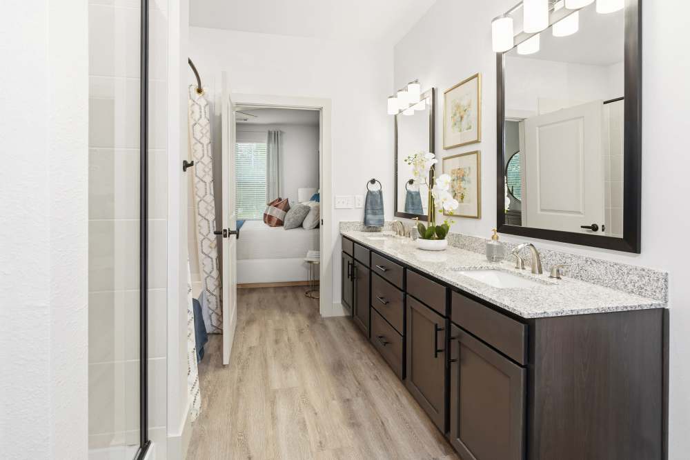 Bathroom with double vanity and granite counters at The Heyward Apartments in Corinth, Texas.