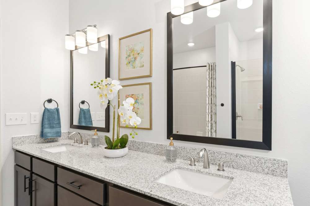 Bathroom vanity with dual sinks and framed mirrors at The Heyward Apartments in Corinth, Texas.