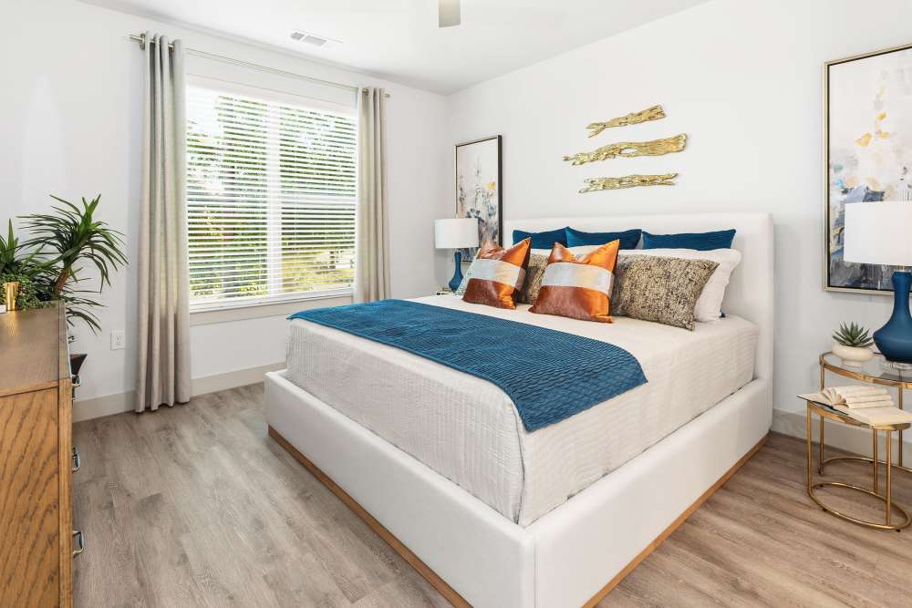 Bedroom with blue accents and large window at The Heyward Apartments in Corinth, Texas.