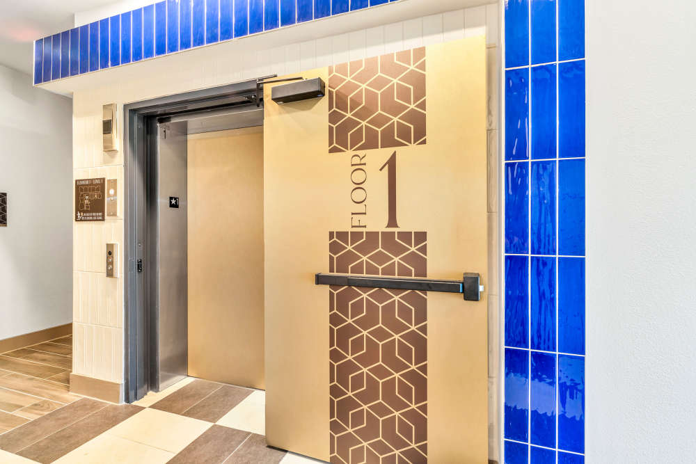 Elevator entrance with gold door and blue tile accents at The Heyward Apartments in Corinth, Texas.
