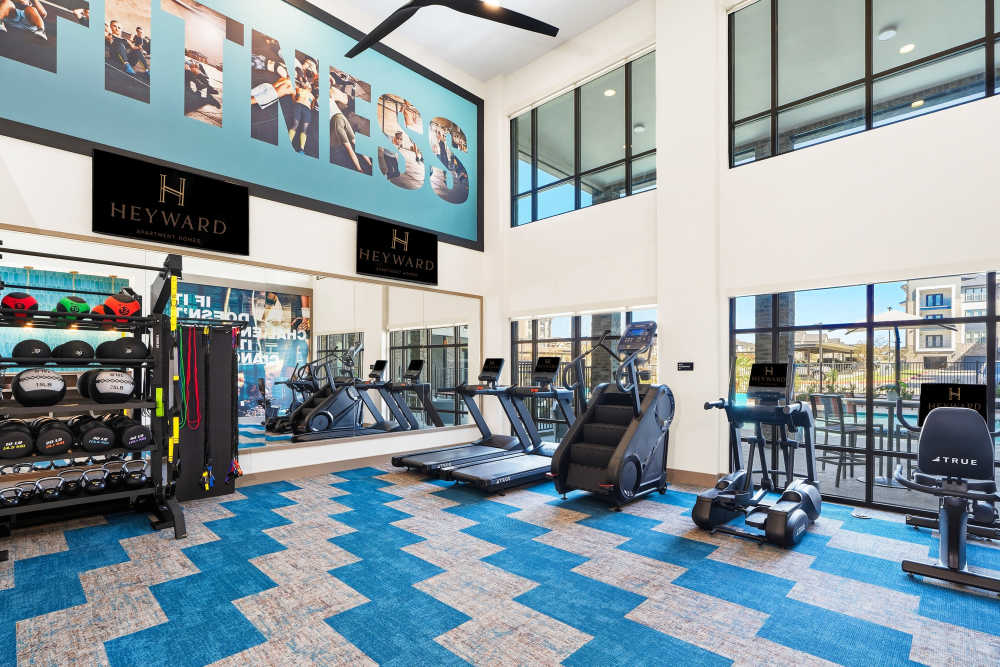 Fitness center with treadmills and large fitness signage at The Heyward Apartments in Corinth, Texas.
