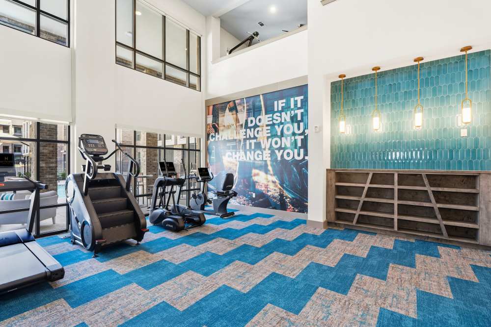 Fitness center with cardio machines and motivational wall art at The Heyward Apartments in Corinth, Texas.