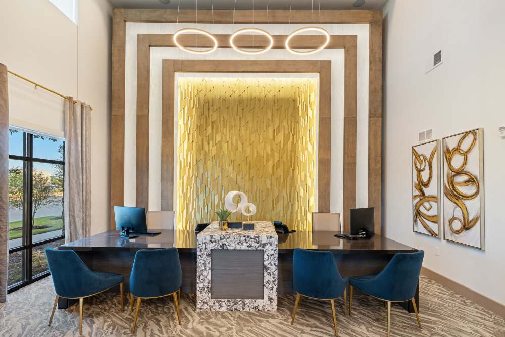 Clubhouse leasing desk with gold textured wall and blue chairs at The Heyward Apartments in Corinth, Texas.