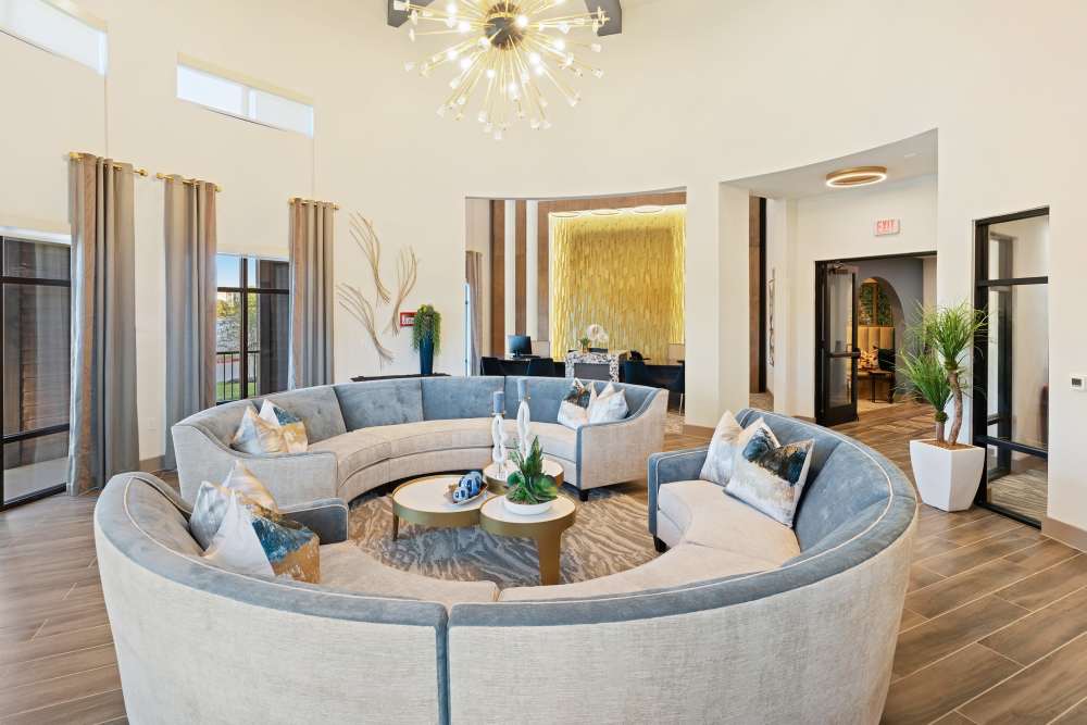 Clubhouse lounge with curved sectional and gold accent wall at The Heyward Apartments in Corinth, Texas.