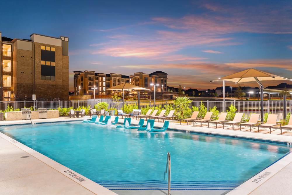 Pool with fountains and sunset lighting at The Heyward Apartments in Corinth, Texas.