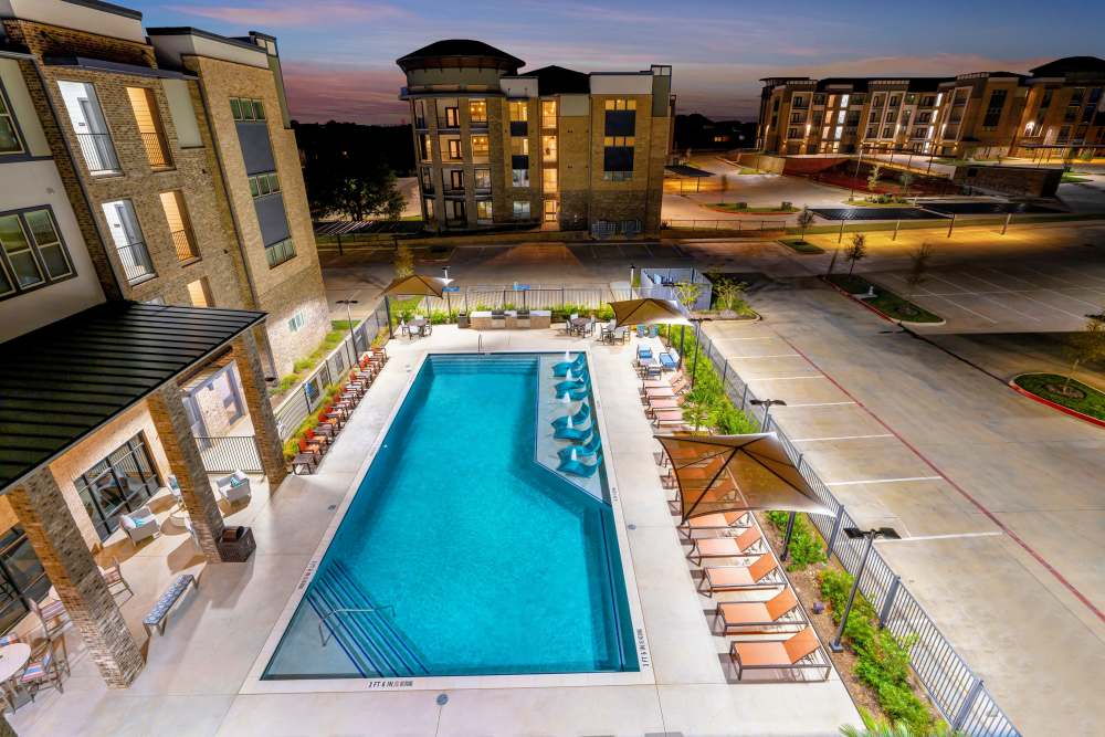 Resort-style pool with lounge chairs and umbrellas at The Heyward Apartments in Corinth, Texas.