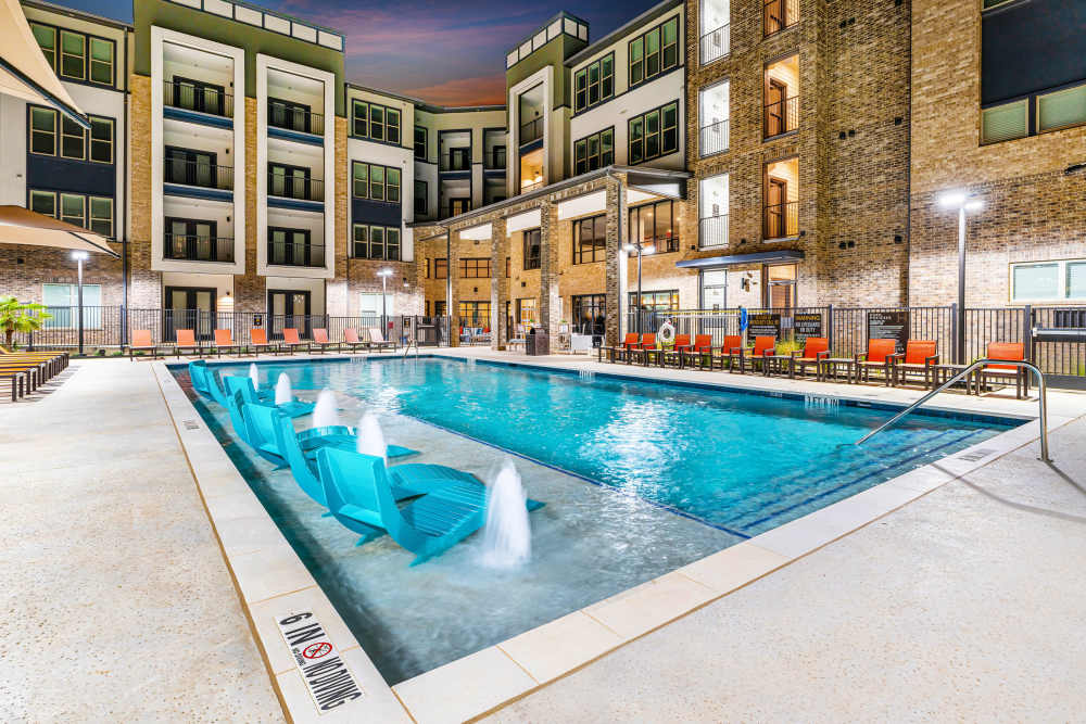 Pool with in-water loungers and fountains at The Heyward Apartments in Corinth, Texas.