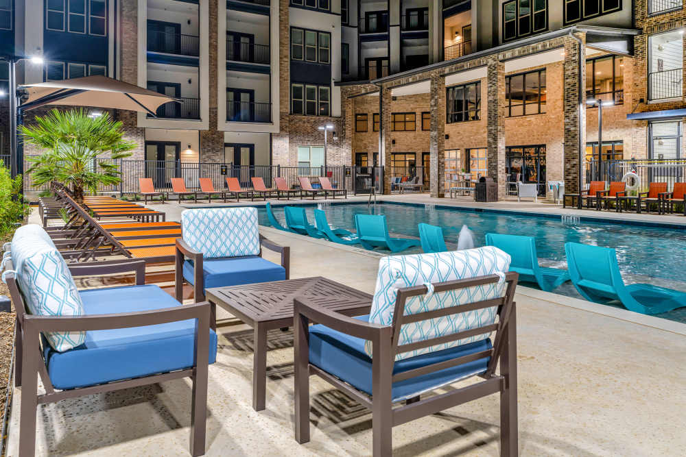 Outdoor seating area by pool with cushioned chairs at The Heyward Apartments in Corinth, Texas.