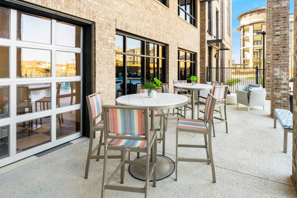 Outdoor patio with high-top tables and chairs at The Heyward Apartments in Corinth, Texas.