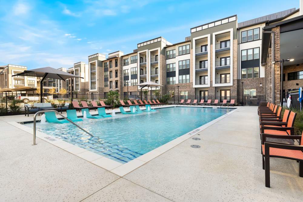Pool with steps and multiple lounge chairs at The Heyward Apartments in Corinth, Texas.