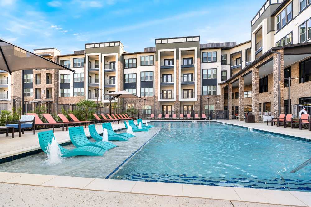 Pool with fountains and shaded lounge chairs at The Heyward Apartments in Corinth, Texas.