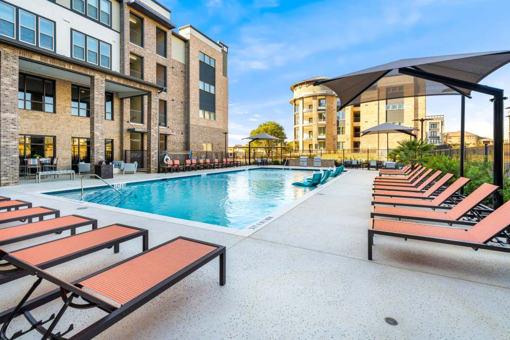 Poolside lounge chairs with umbrellas and open view at The Heyward Apartments in Corinth, Texas.