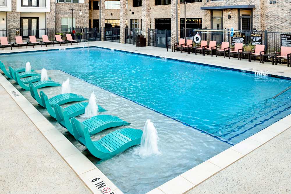 Resort-style pool with in-water loungers and fountains at The Heyward Apartments in Corinth, Texas.