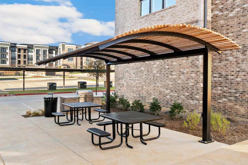 Outdoor picnic area with covered tables and benches at The Heyward Apartments in Corinth, Texas.
