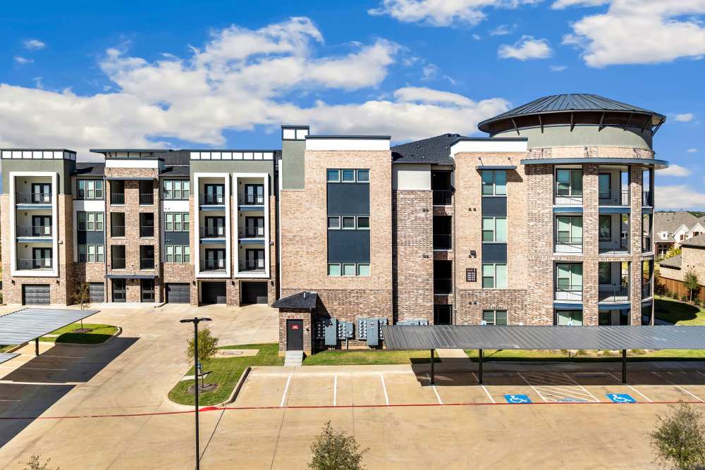 Apartment building with covered parking spaces at The Heyward Apartments in Corinth, Texas.