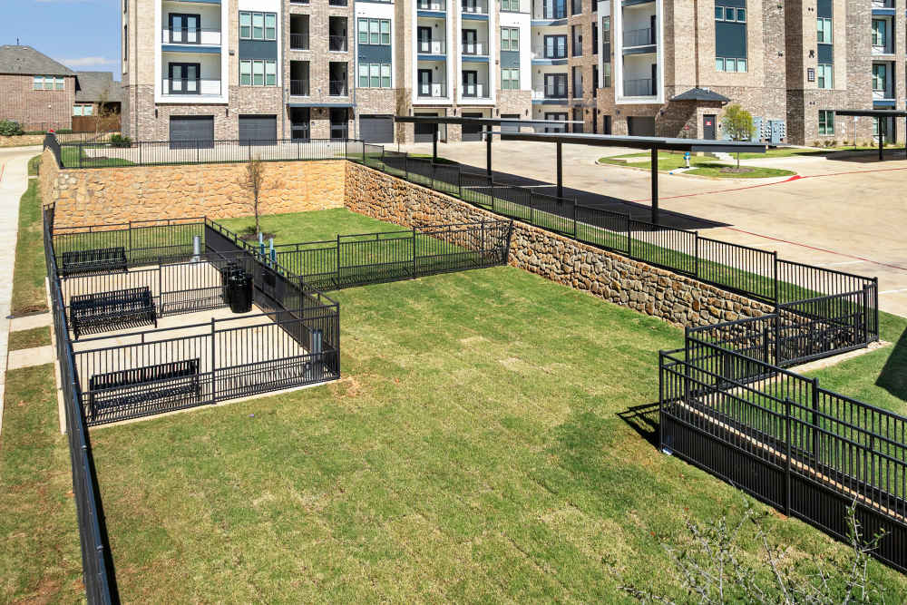 Fenced dog park with benches and green lawn at The Heyward Apartments in Corinth, Texas.