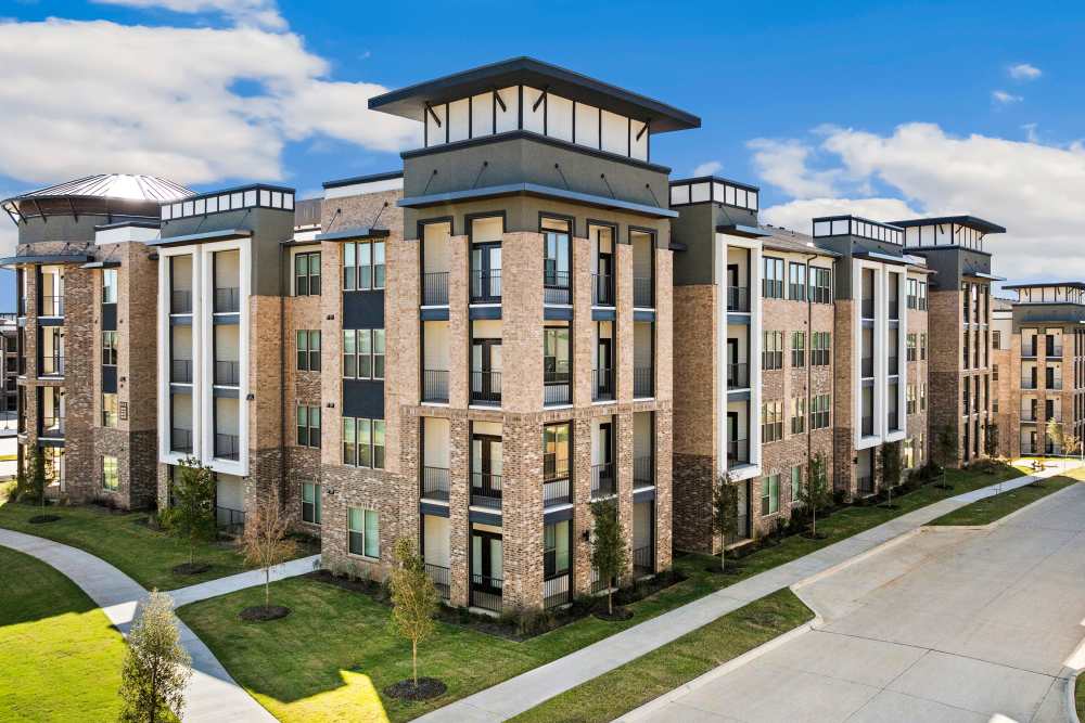 Corner view of apartment building with landscaped walkway at The Heyward Apartments in Corinth, Texas.