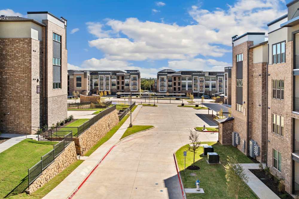 View between apartment buildings showing driveway and parking at The Heyward Apartments in Corinth, Texas.