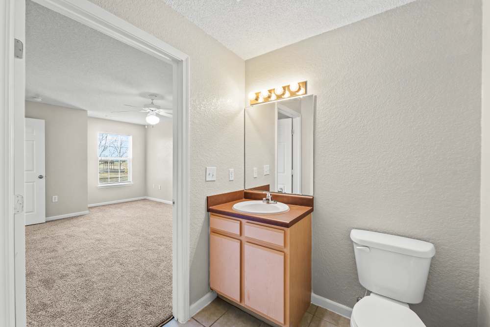 Bathroom with single-sink vanity, mirror, toilet, and view into carpeted bedroom at Callaway Village Apartments in Fulton, Missouri