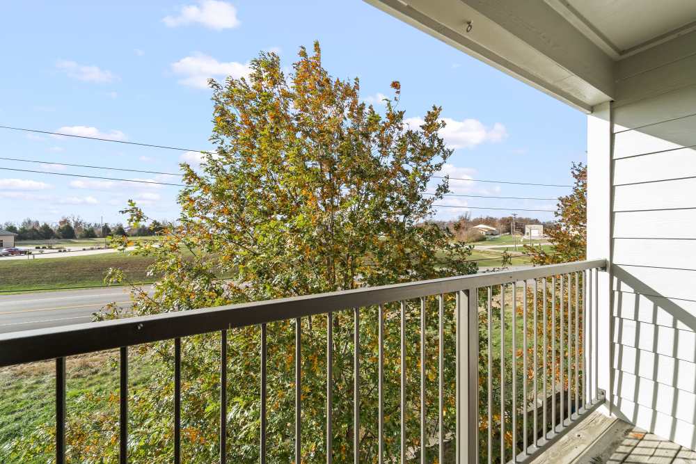 Balcony view with metal railing, autumn tree, road, and clear sky with scattered clouds at Callaway Village Apartments in Fulton, Missouri