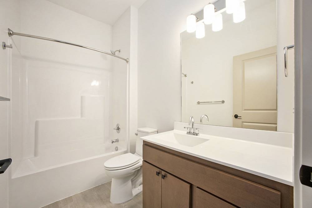 Bathroom with white tub and shower combo, large mirror, and wood vanity under bright lighting at Terra Station, Hudsonville, Michigan