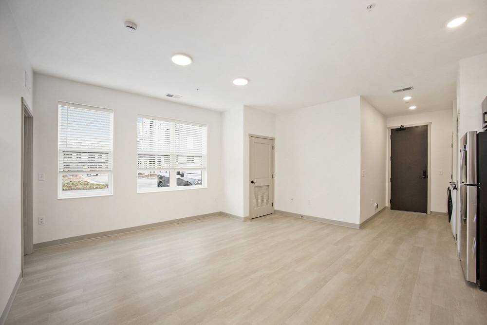 Open living space with light wood flooring, large windows, and entry door near kitchen at Terra Station, Hudsonville, Michigan