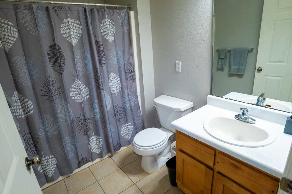 Bathroom with tile flooring, commode and tub with curtain at Hampton Village in Palestine, Texas