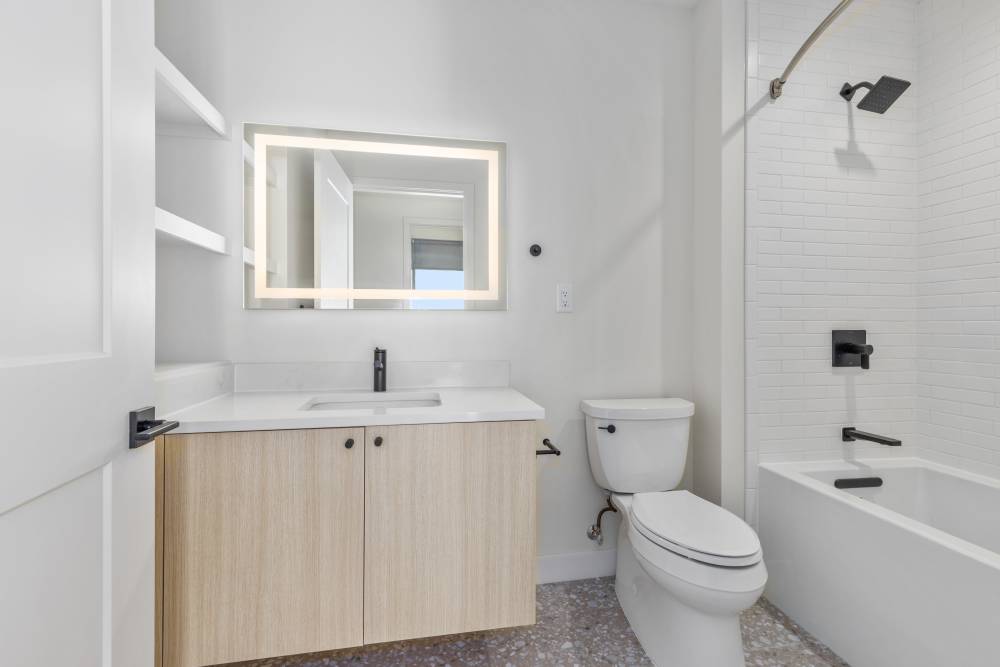 Bathroom with light wood vanity, white tile tub, and black fixtures at Studio Park Tower & Lofts in Grand Rapids, Michigan