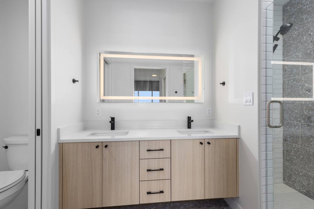 Bathroom with dual sinks, LED mirror, and glass shower at Studio Park Tower & Lofts in Grand Rapids, Michigan