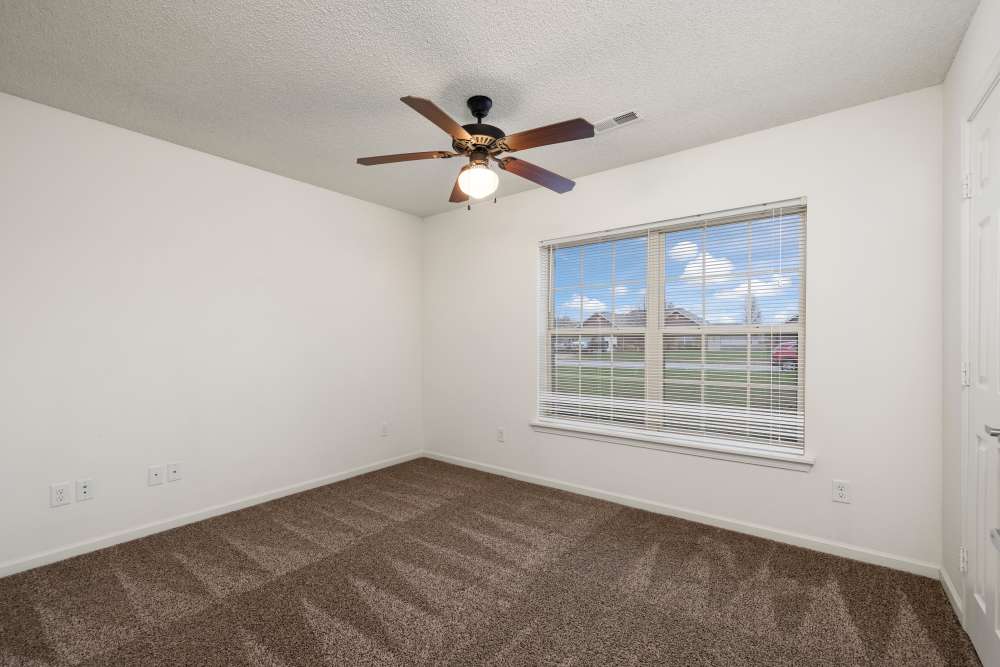 Unfurnished bed room with carpet flooring , ceiling fan, and large window at Oaklawn II in Rogersville, Missouri 