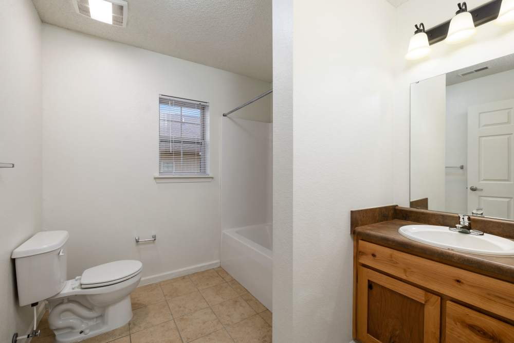 Bathroom with white toilet, bathtub, wooden vanity, and large mirror at Oaklawn II in Rogersville, Missouri 