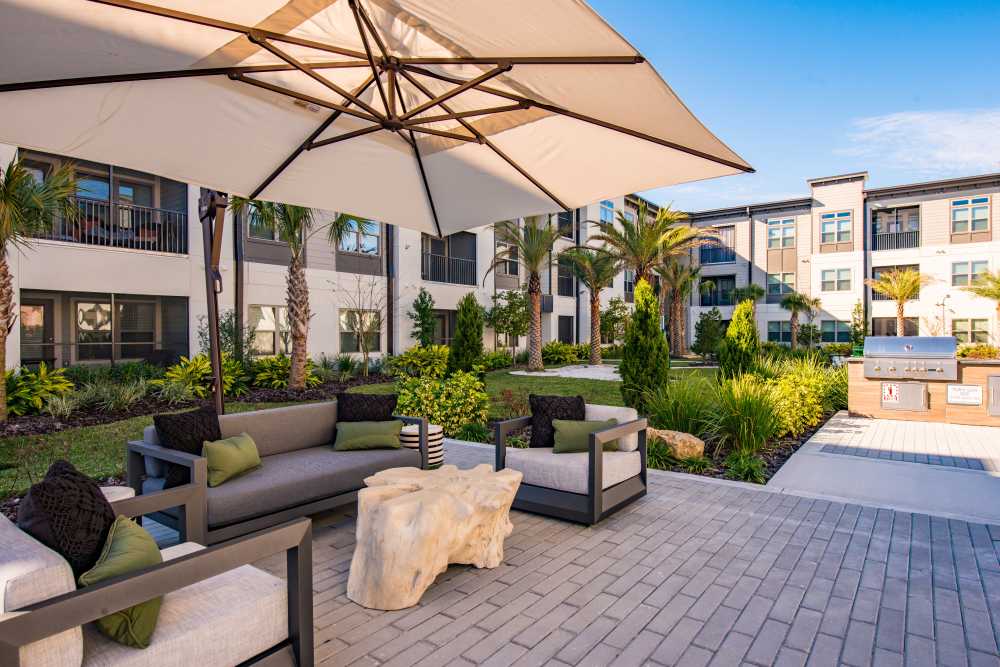 Outdoor courtyard with cushioned seating under a large umbrella, surrounded by palm trees at The Walton in Sanford, Florida.